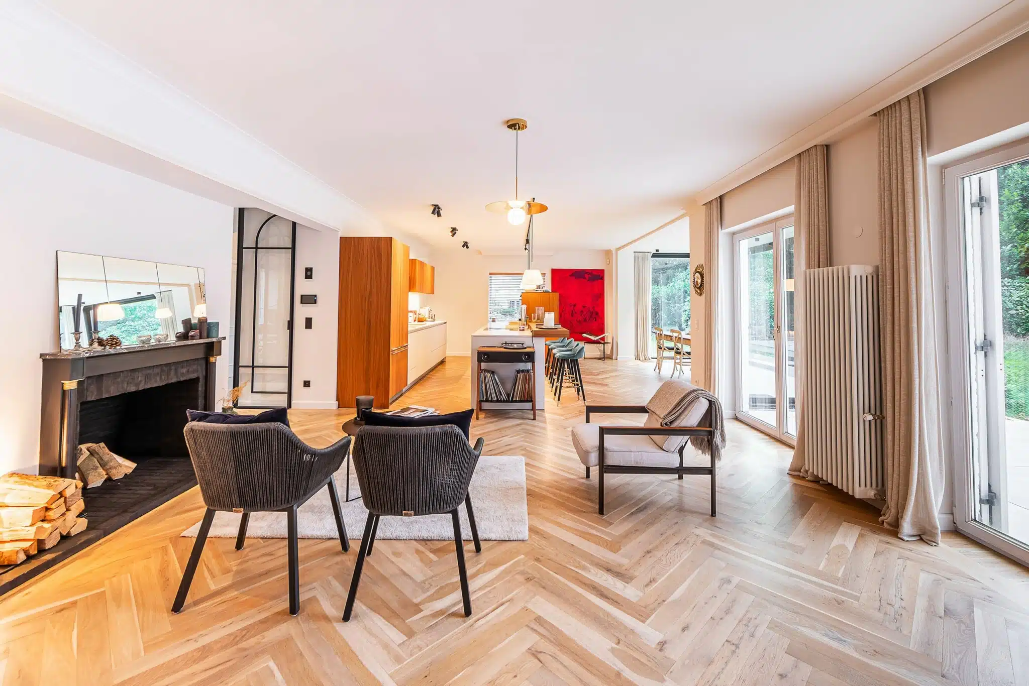 Salon moderne lumineux avec mur rouge, parquet en chevron, mobilier élégant et cuisine en bois.
