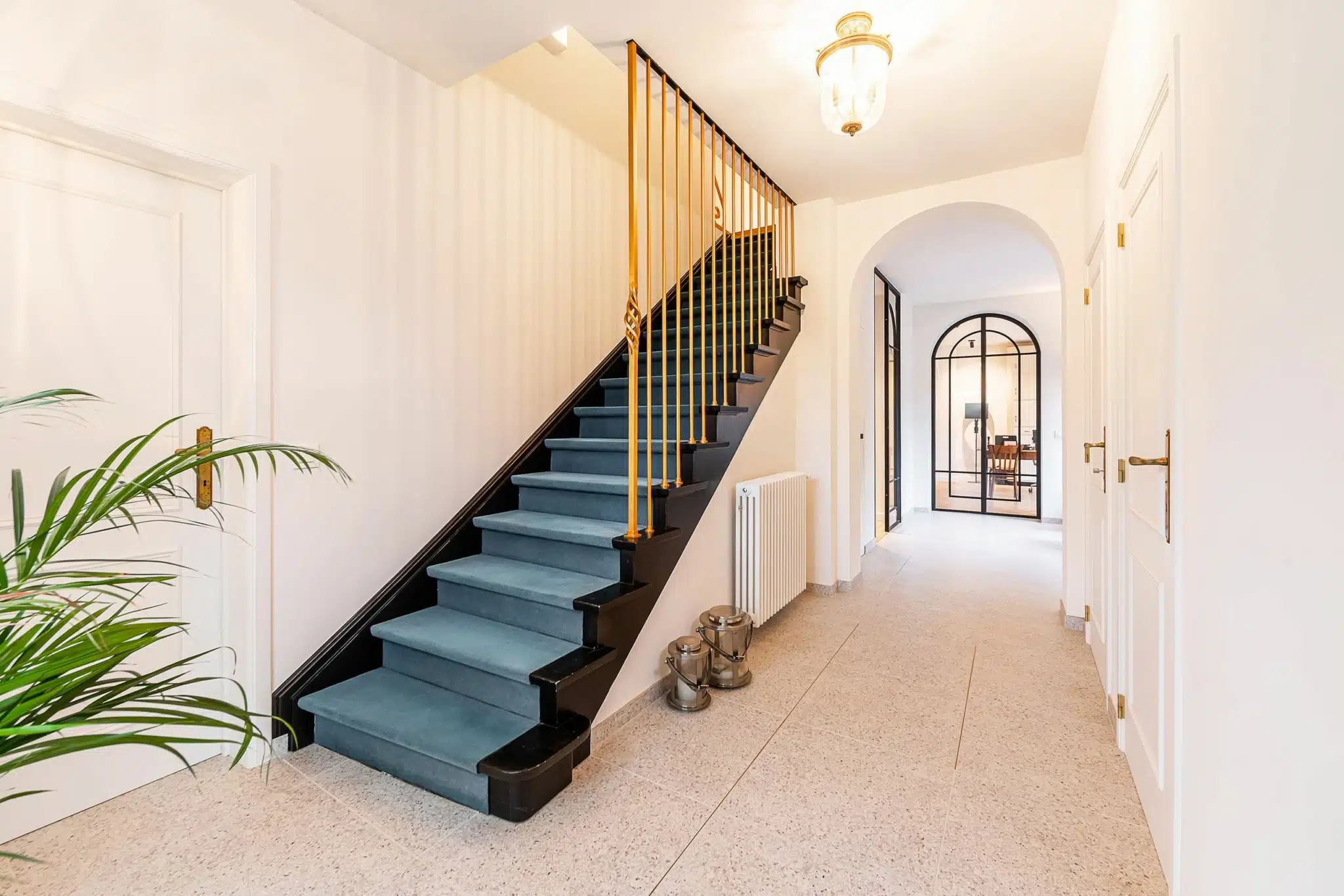 Entrée lumineuse avec escalier bleu, rampe élégante, décoration florale et espace ouvert.