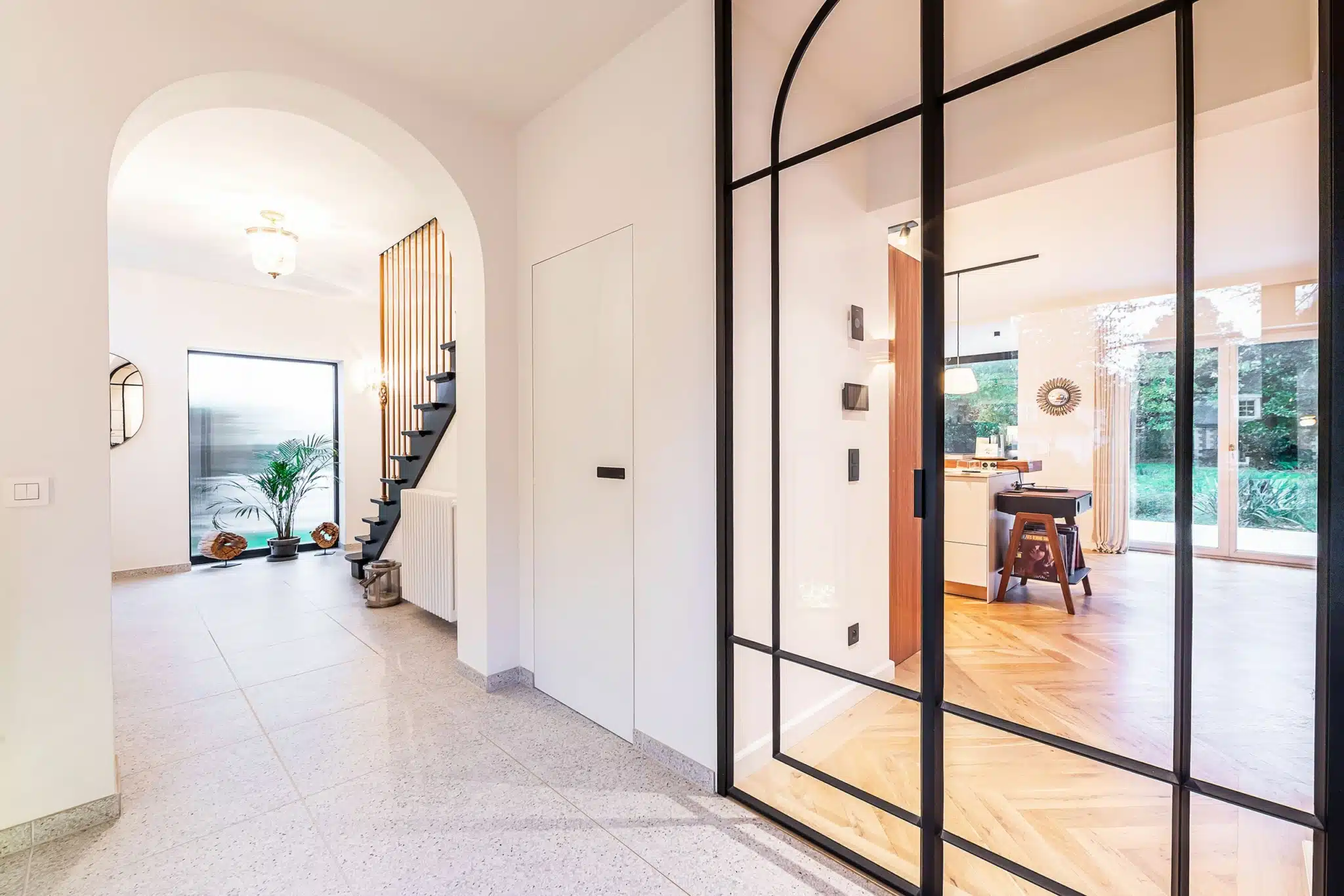 Entrée moderne avec escalier en bois, verrière en verre noir, ambiance lumineuse et élégante.