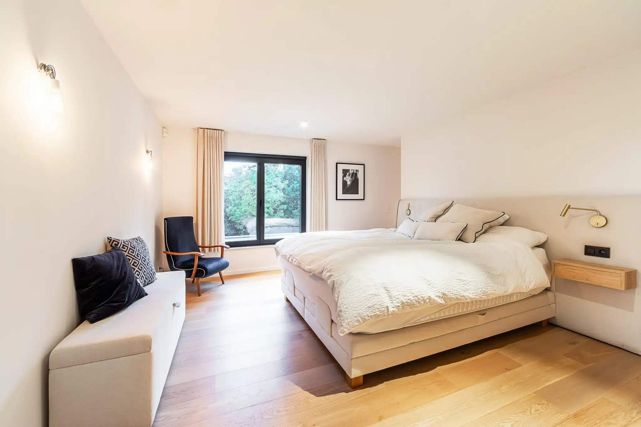 Chambre moderne avec vue sur la nature, grand lit, coin cosy, lumière naturelle, décoration minimaliste.