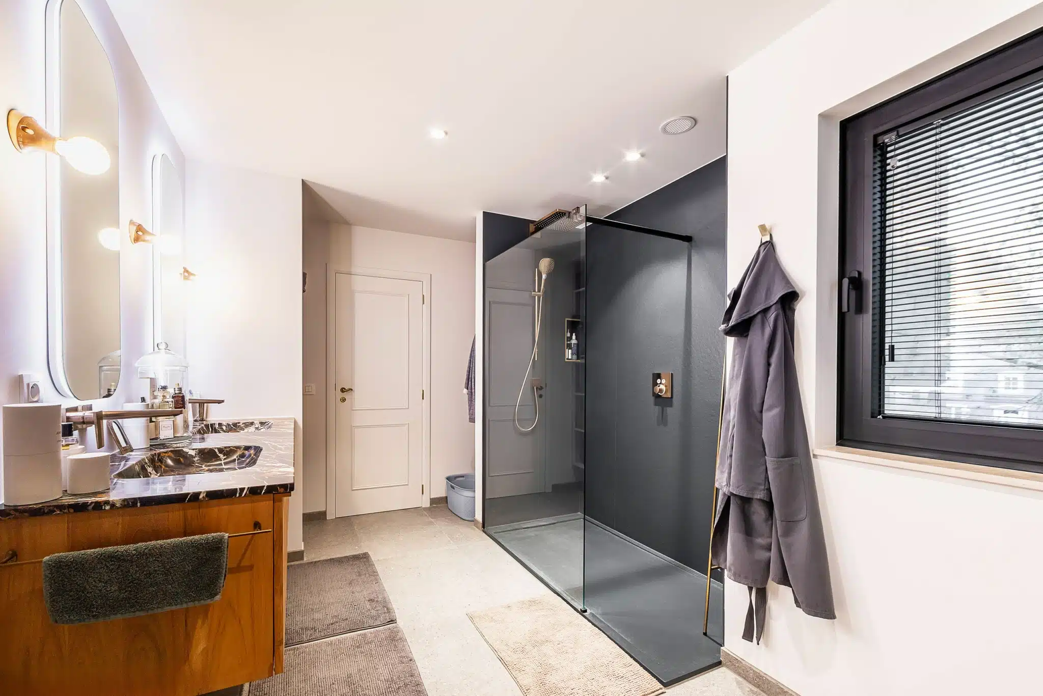 Salle de bain moderne avec douche en verre noire, meuble en bois, miroir rond, ambiance élégante.