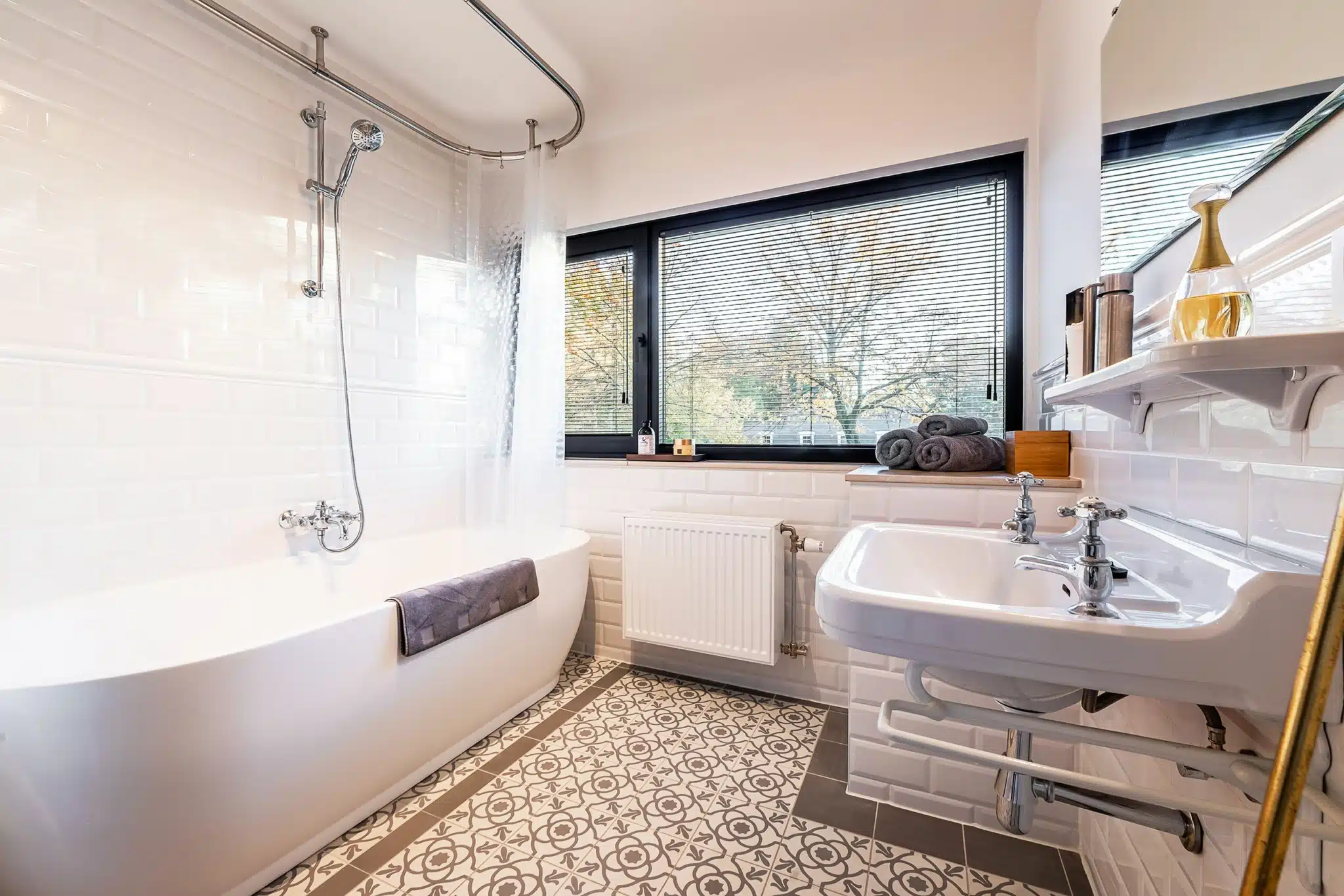 Salle de bain moderne avec baignoire blanche, grande fenêtre et sol en carreaux design.