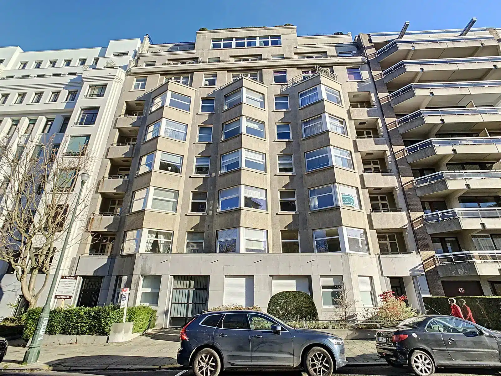 Résidence moderne avec balcons, grandes fenêtres et voitures stationnées dans un environnement urbain dynamique.