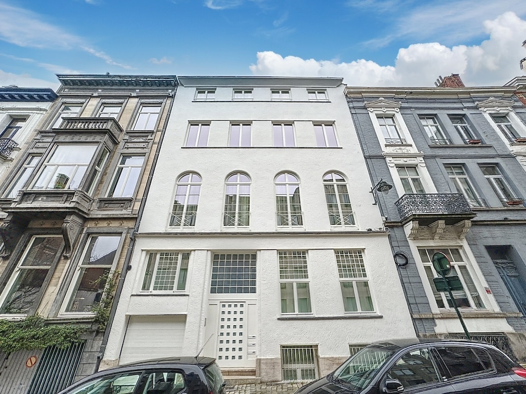 Bâtiment moderne blanc avec grandes fenêtres archaisées, harmonie urbaine entre style traditionnel et contemporain.