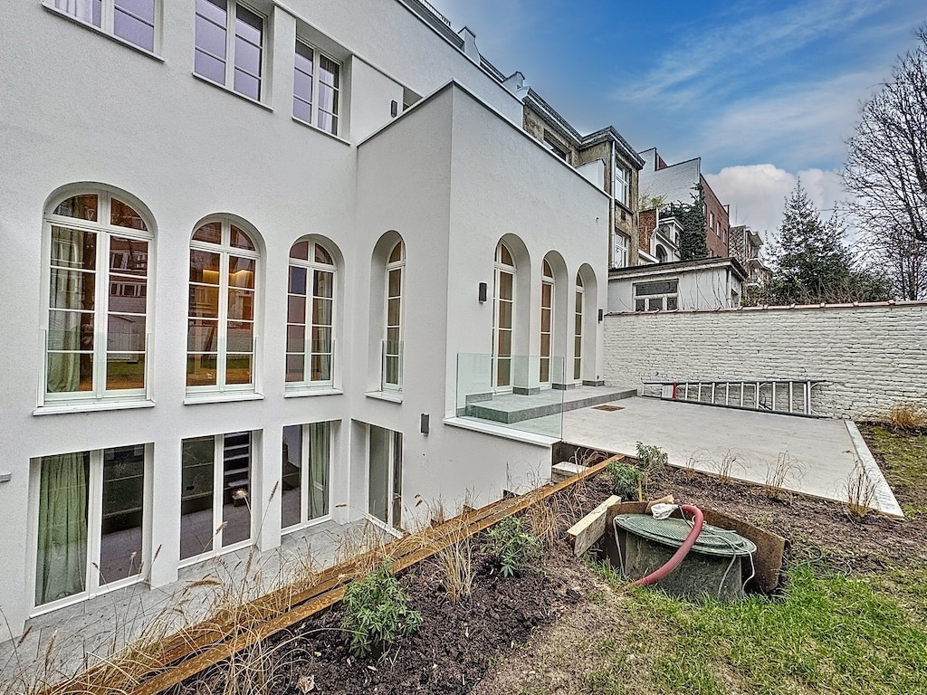 Maison moderne avec grandes fenêtres, jardin en cours d’aménagement, façade blanche, ambiance lumineuse.