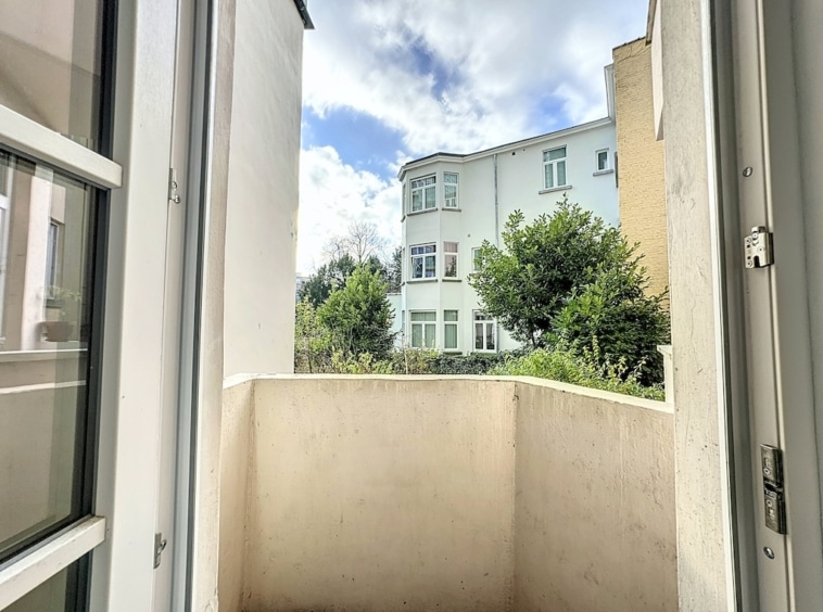 Balcon avec vue sur un quartier résidentiel verdoyant sous un ciel nuageux lumineux.