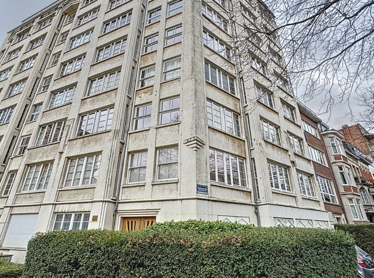 Bâtiment moderne avec grandes fenêtres, façade géométrique, jardin urbain et environnement dynamique.