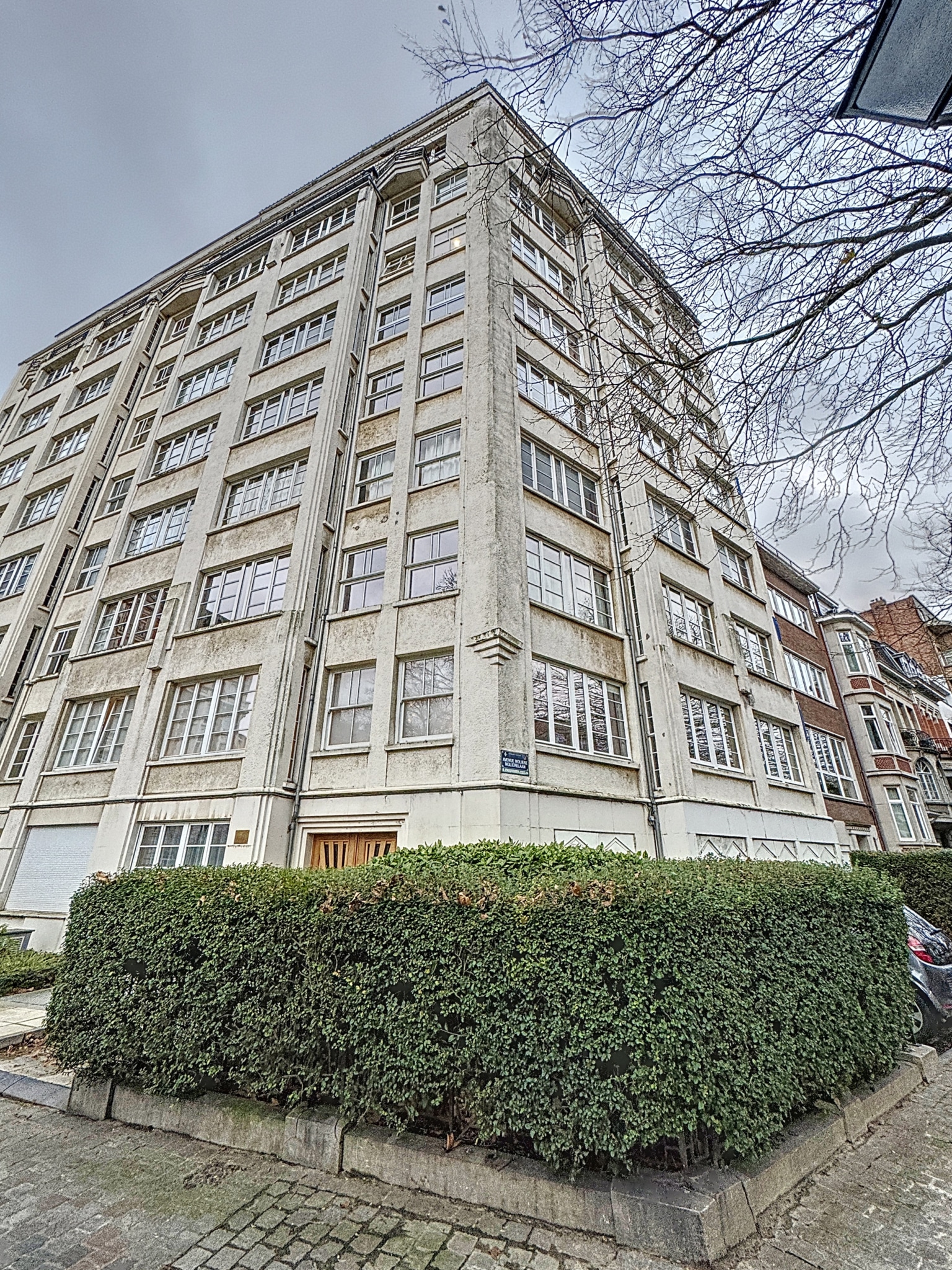 Bâtiment moderne avec grandes fenêtres, façade géométrique, jardin urbain et environnement dynamique.