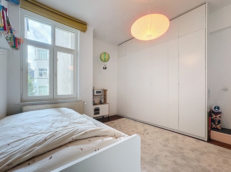 Chambre minimaliste lumineuse avec rangement intégré, lit blanc, fenêtres nature, décoration moderne.