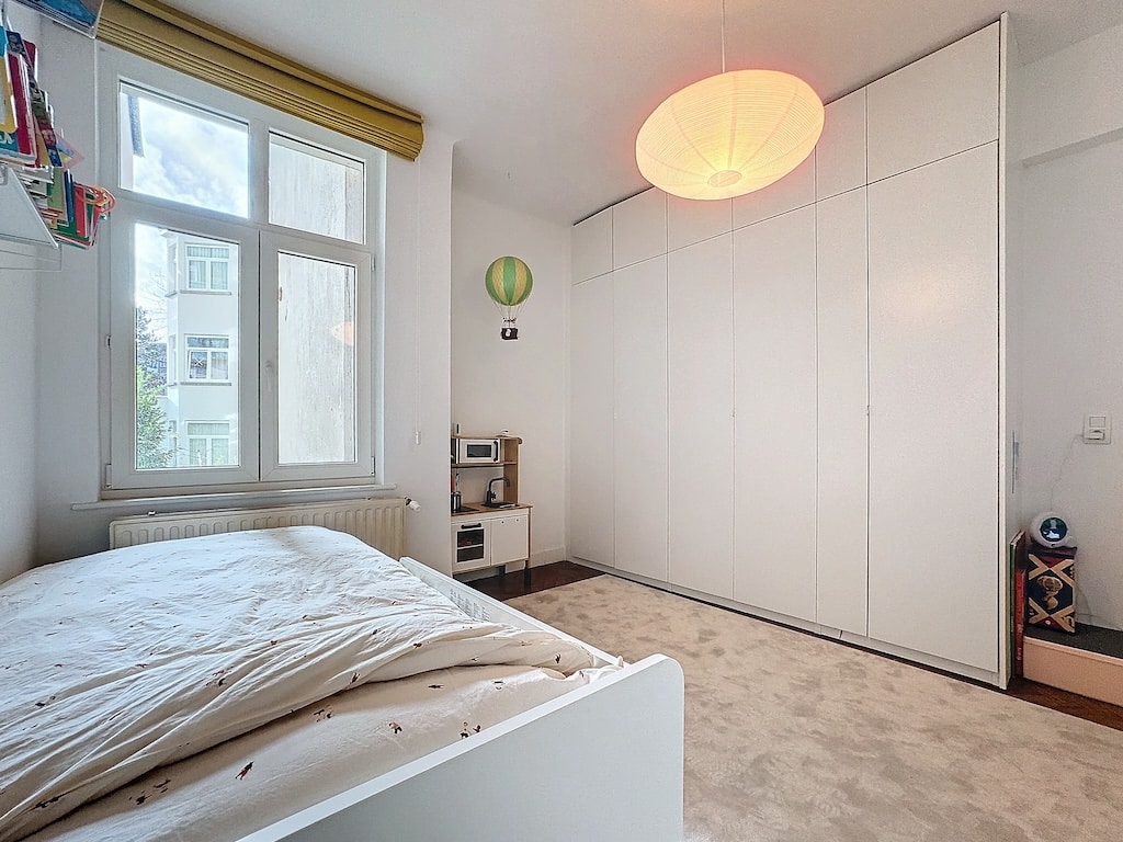 Chambre minimaliste lumineuse avec rangement intégré, lit blanc, fenêtres nature, décoration moderne.