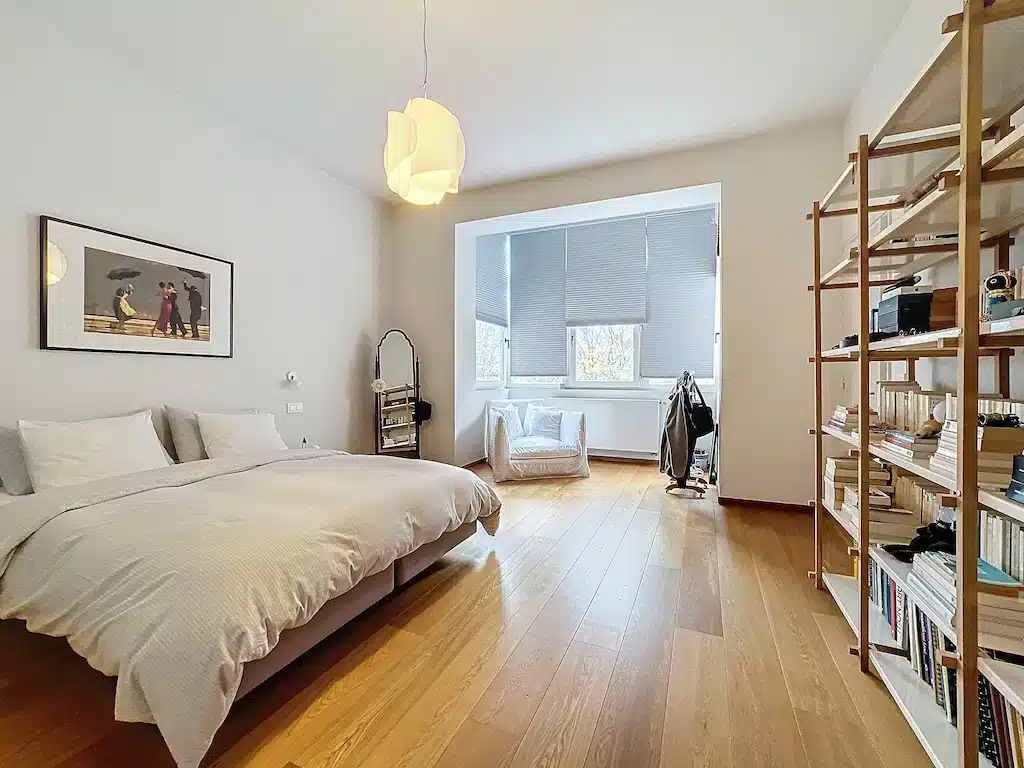 Chambre minimaliste lumineuse avec lit gris, coin lecture cosy, bibliothèque en bois, ambiance apaisante.