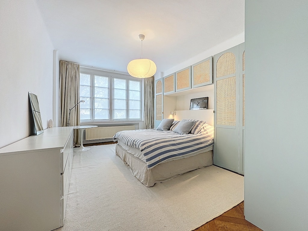Chambre moderne lumineuse avec lit gris, décoration épurée et ambiance relaxante.