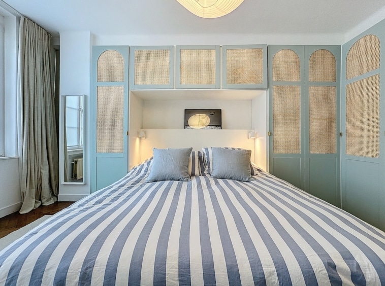 Chambre élégante et zen avec lit à rayures, mobilier en rotin, luminaires chaleureux et lumière naturelle.