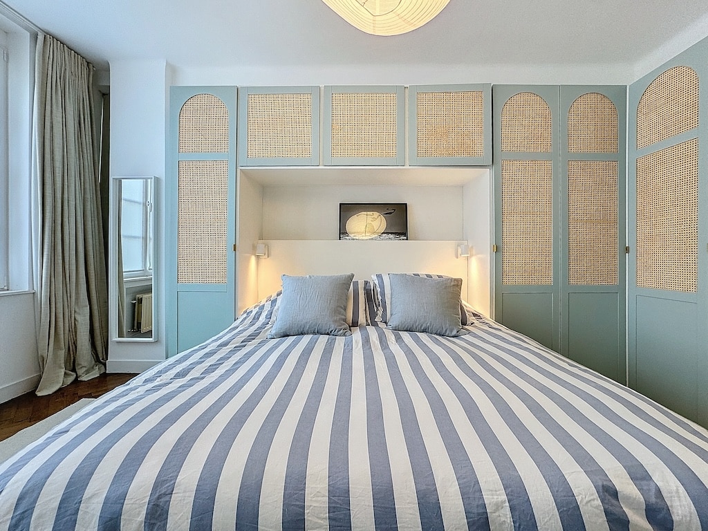 Chambre élégante et zen avec lit à rayures, mobilier en rotin, luminaires chaleureux et lumière naturelle.
