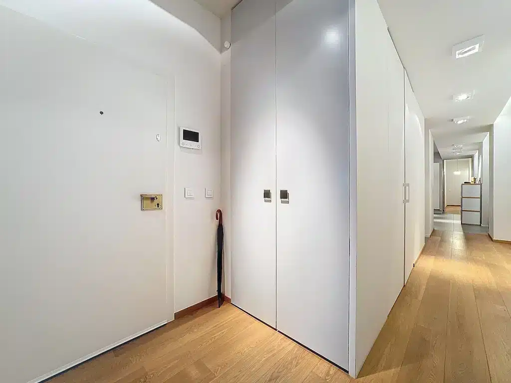Couloir moderne avec portes blanches, sol en bois, éclairage doux et gestion intelligente.