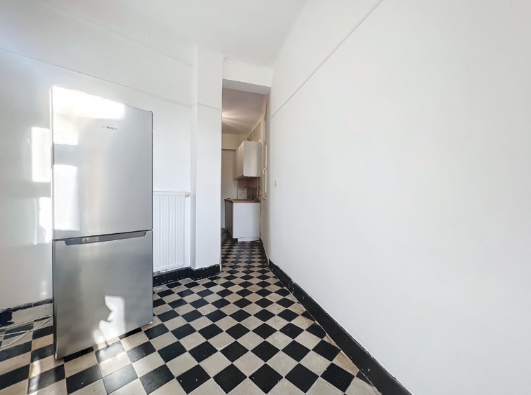 Cuisine moderne blanche avec sol à carreaux noir et blanc, réfrigérateur inox, espace pratique et lumineux.