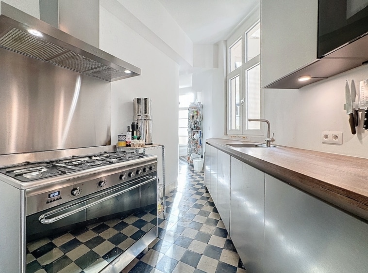 Cuisine moderne avec plan en bois, sol à carreaux noirs et blancs, lumineux et élégante.