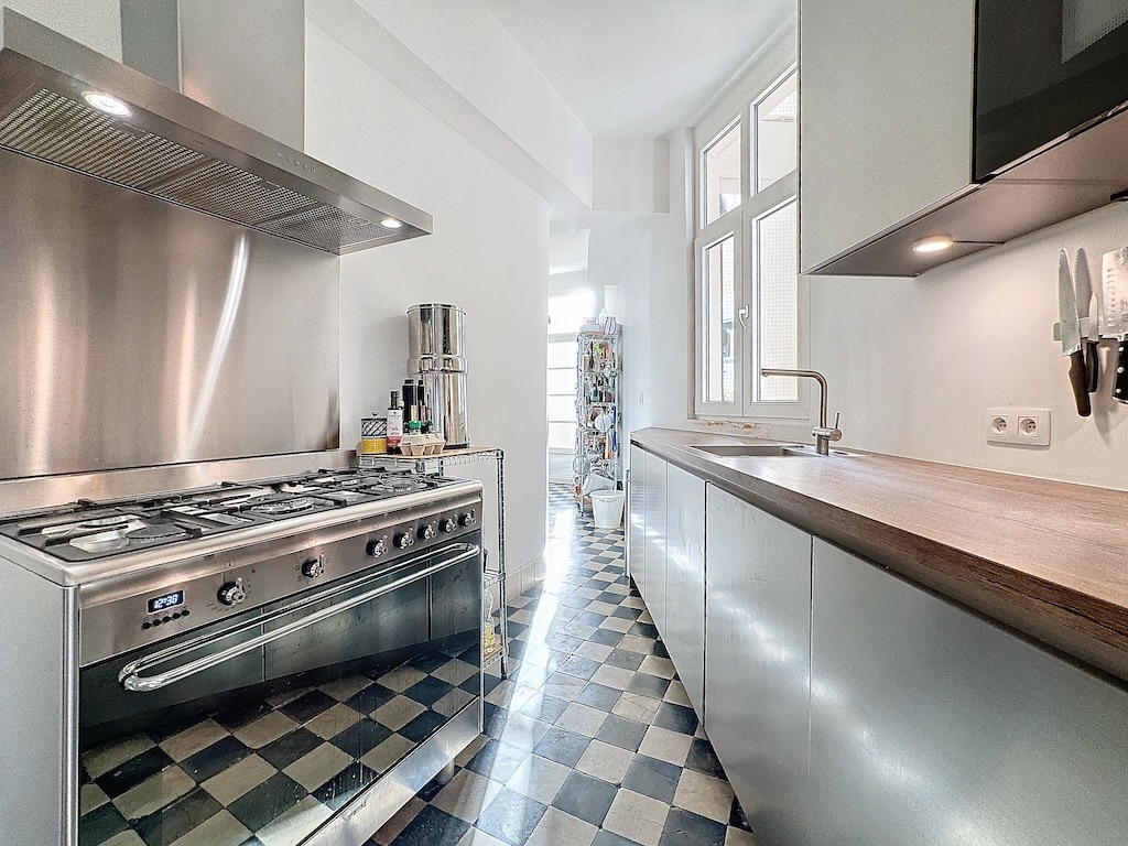 Cuisine moderne avec plan en bois, sol à carreaux noirs et blancs, lumineux et élégante.