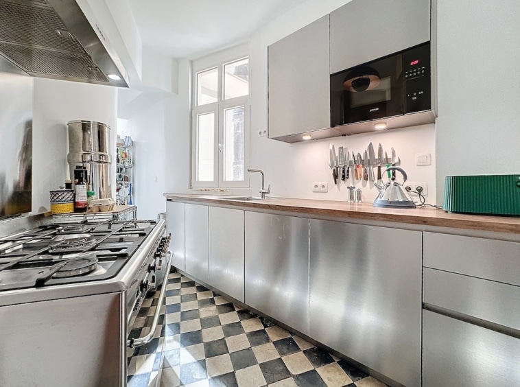Cuisine moderne en acier inoxydable avec sol noir et blanc, éclairée par une grande fenêtre.