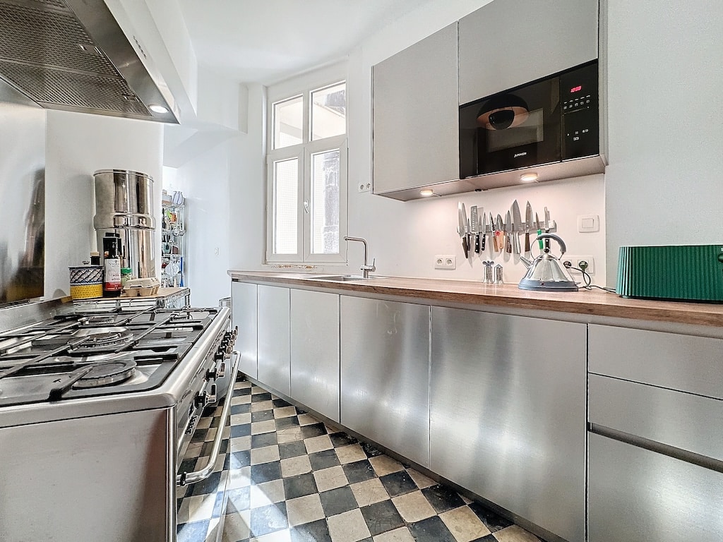 Cuisine moderne en acier inoxydable avec sol noir et blanc, éclairée par une grande fenêtre.