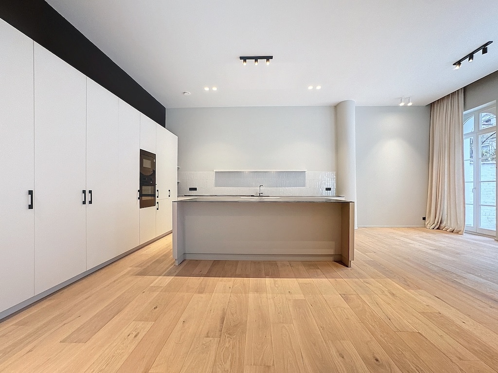 Cuisine moderne lumineuse avec îlot en pierre, armoires épurées, grand espace ouvert design.