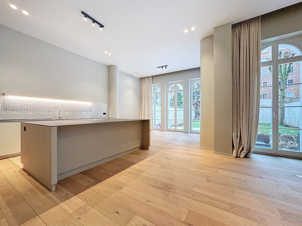 Cuisine moderne lumineuse avec îlot, large fenêtres, sols en bois clair et espace convivial.