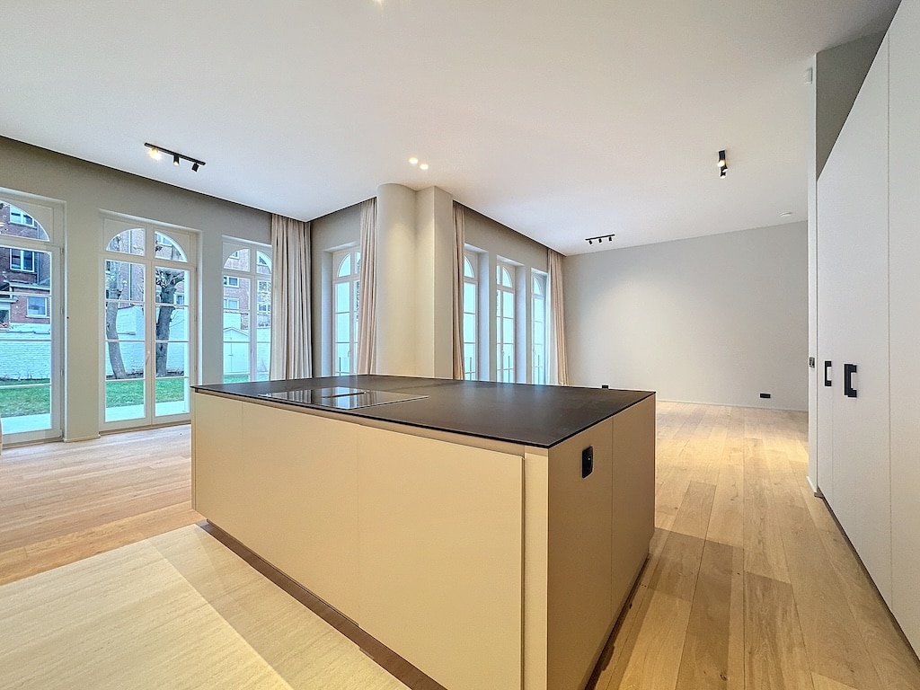 Cuisine moderne lumineuse avec grand îlot en quartz, large baie vitrée et sol en bois chaleureux.