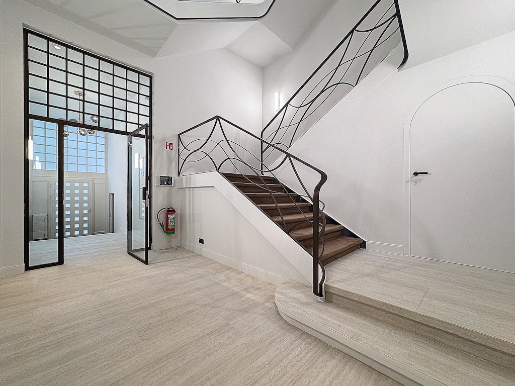 Entrée moderne avec escalier courbé en bois, rampe géométrique, murs blancs lumineux, ambiance élégante.