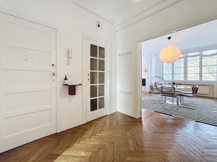 Espace dentrée moderne lumineux avec portes en verre et salon élégant au parquet en chevrons.