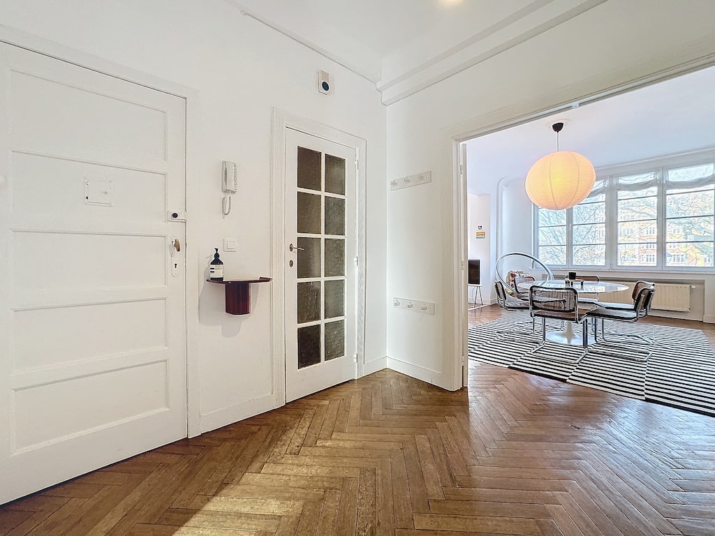 Espace dentrée moderne lumineux avec portes en verre et salon élégant au parquet en chevrons.