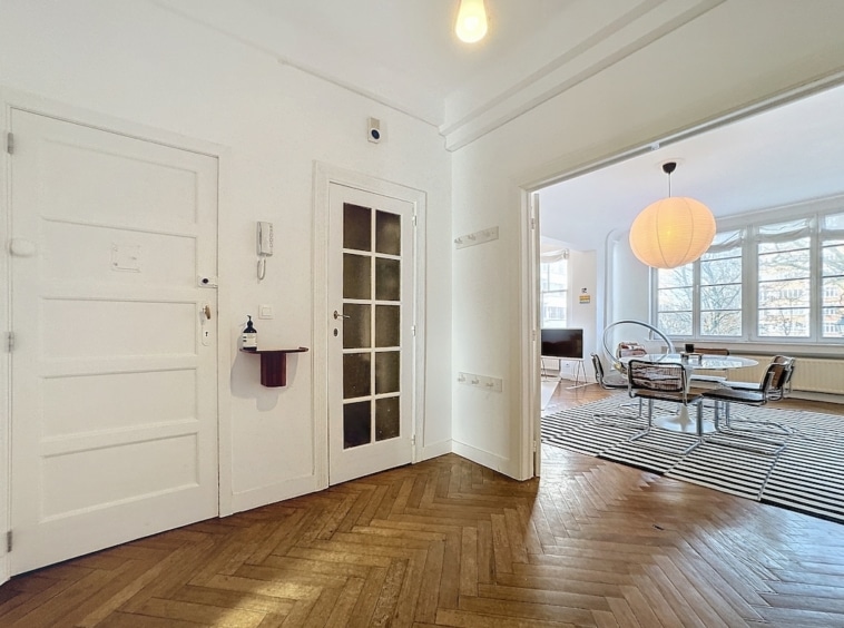 Entrée moderne avec parquet en chevrons, portes en verre et salon lumineux lumineux.