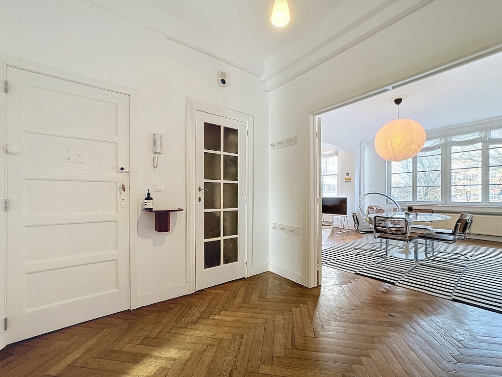 Entrée moderne avec parquet en chevrons, portes en verre et salon lumineux lumineux.