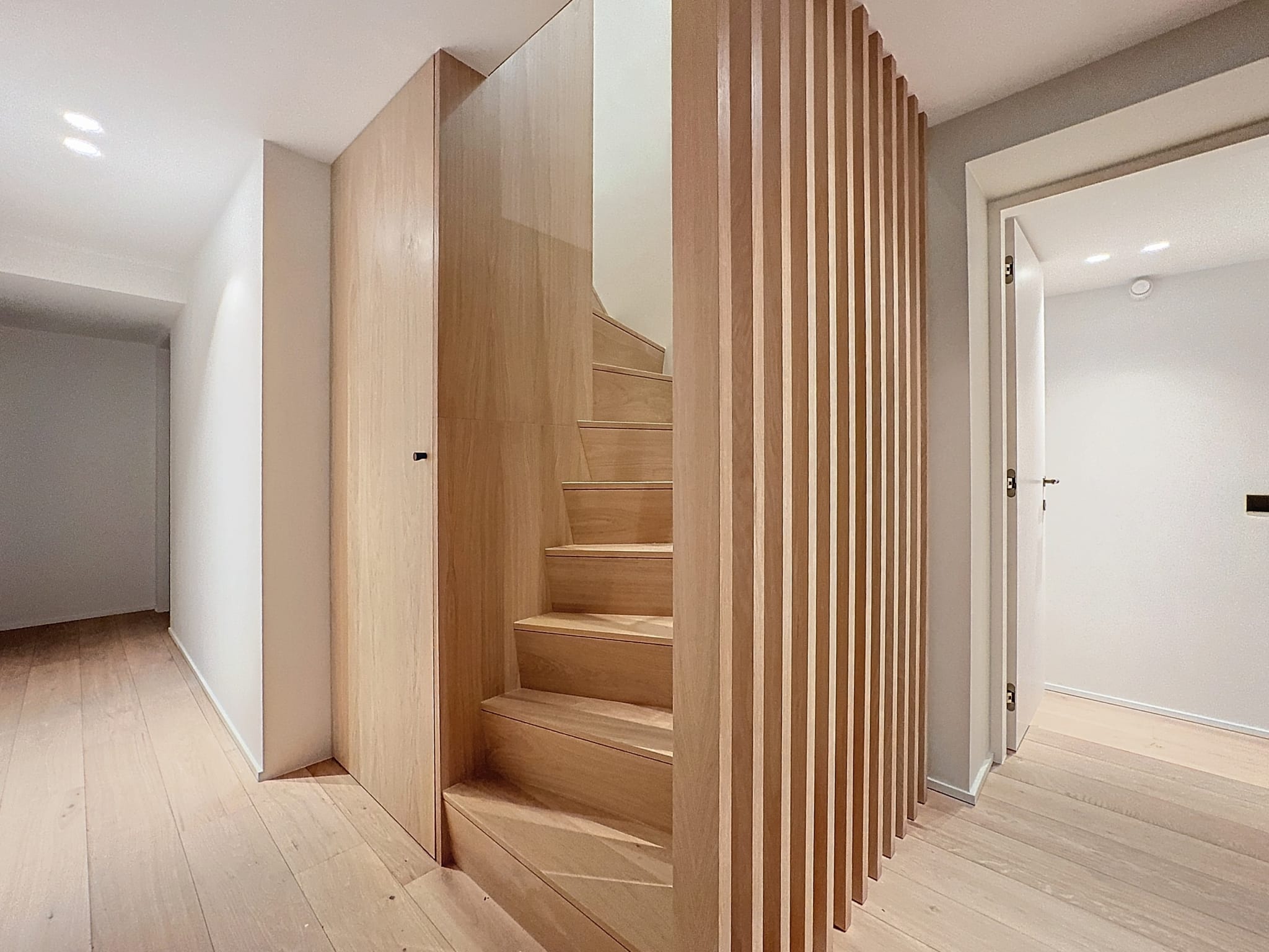 Couloir moderne en bois clair, lumineux et minimaliste avec escalier à lattes horizontales élégantes.