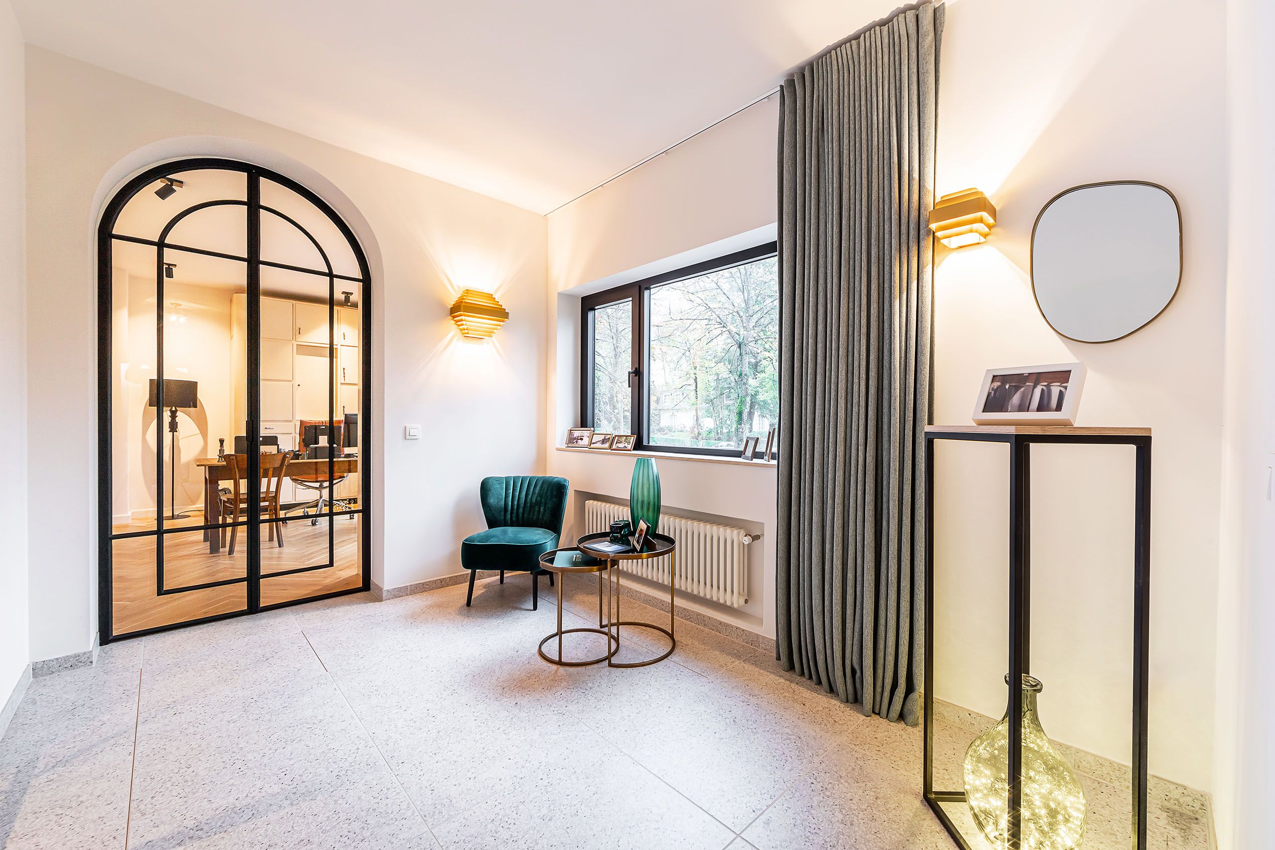 Intérieur moderne lumineux avec porte arc en verre, fauteuil vert, table noire et miroir élégant.