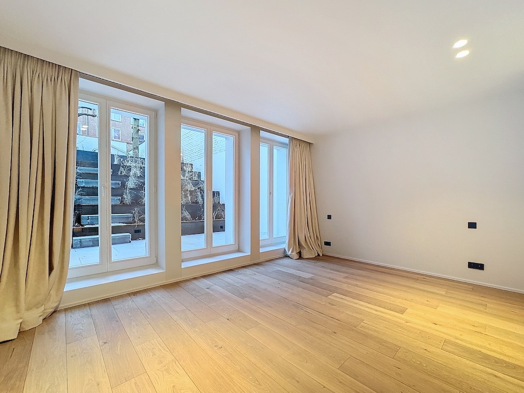 Espace minimaliste lumineux avec grandes fenêtres, murs neutres, sol en bois clair et ambiance moderne.