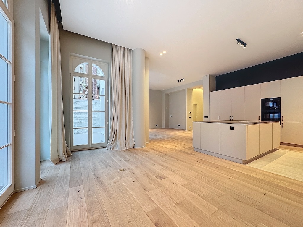 Salon moderne lumineux avec cuisine épurée, grandes fenêtres, bois clair et design contemporain.