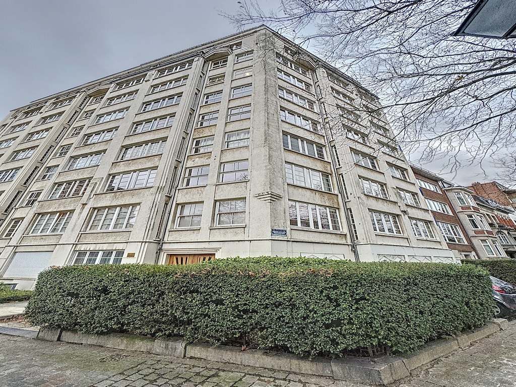 Résidence classique au coin de la rue Pesante, façades beiges, balcons, entourée d’une haie soignée.