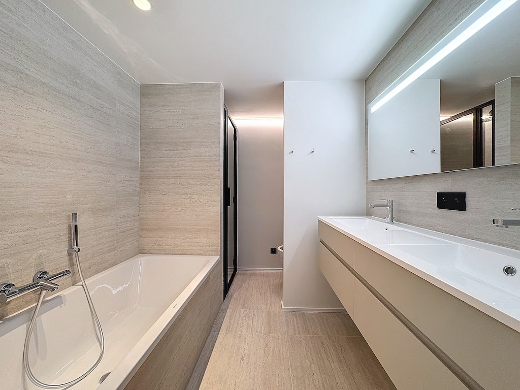 Salle de bain moderne avec baignoire, douche en verre, grand miroir, design épuré et lumineux.