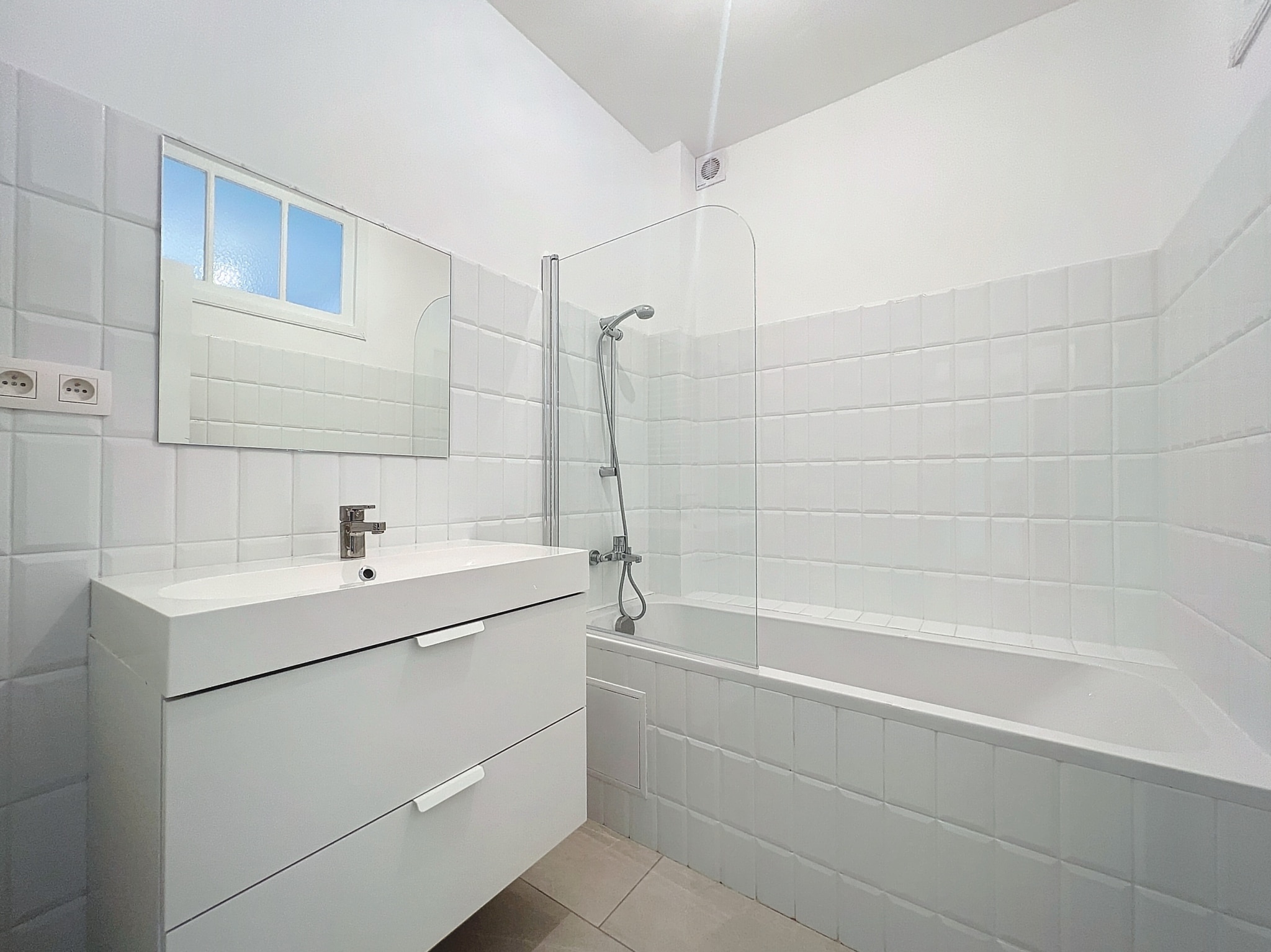 Salle de bain moderne lumineuse avec douche, baignoire, meuble blanc et design minimaliste.
