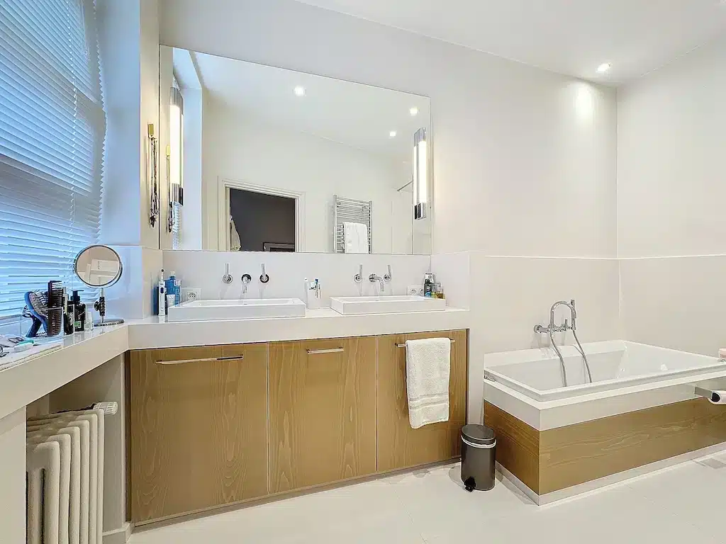 Salle de bain moderne lumineuse avec double lavabo, baignoire élégante et rangements en bois clair.