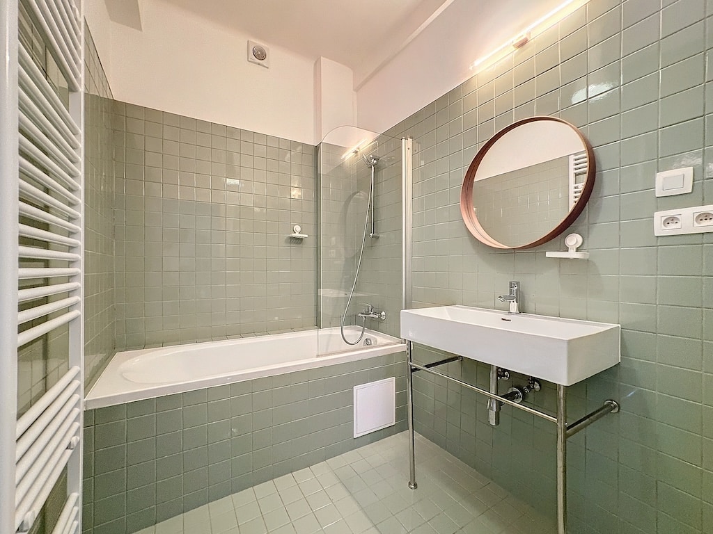 Salle de bain moderne avec baignoire blanche, lavabo suspendu, miroir en bois et ambiance pastel.