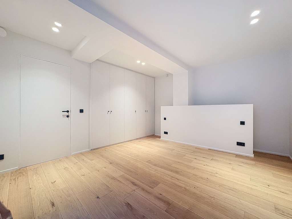 Salon moderne minimaliste avec rangements intégrés, murs clairs, sol en bois, ambiance épurée et élégante.