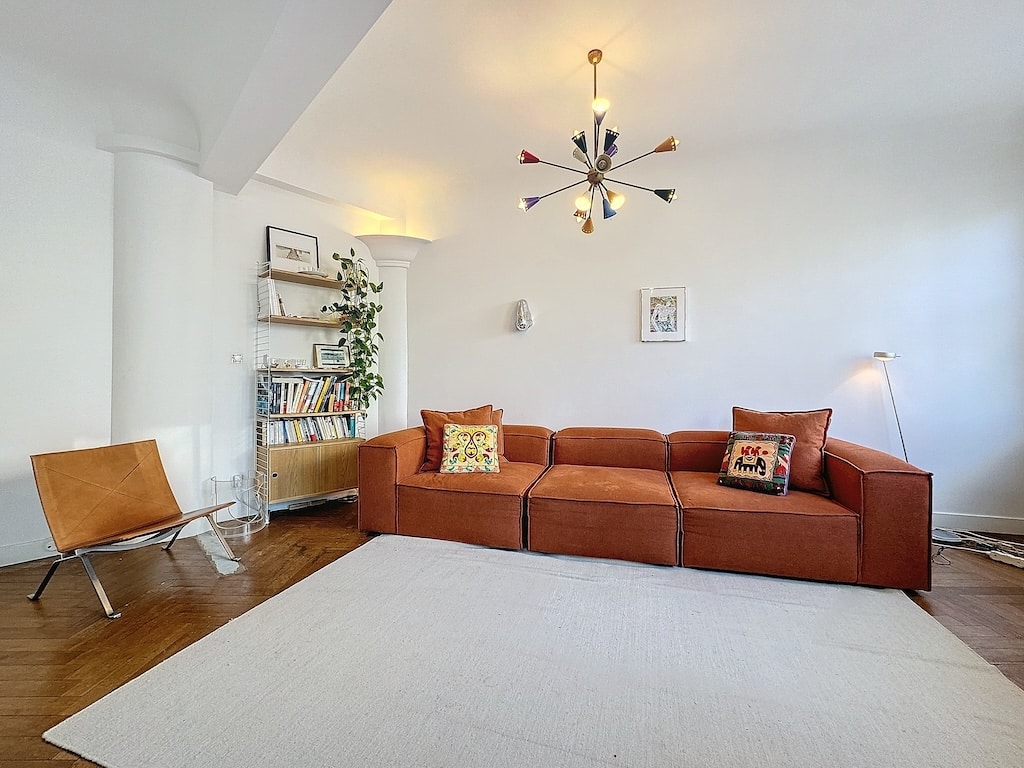 Salon moderne avec canapé orange, tapis clair, éclairage coloré et bibliothèque chaleureuse.