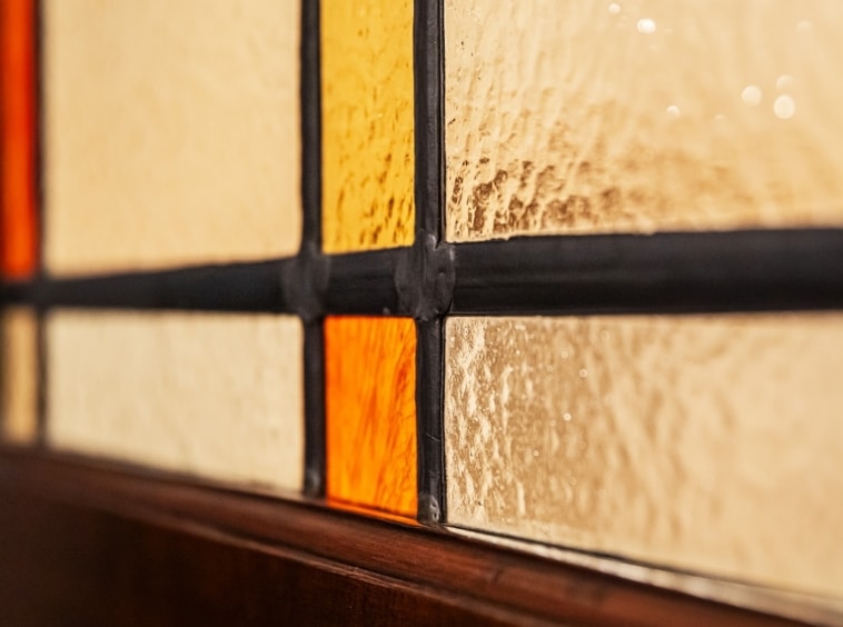 Vitrail coloré en amber, reflet lumineux, encadre métallique sombre, ambiance chaleureuse et artisanale.