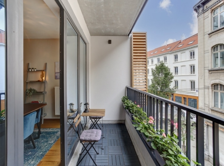 Balcon moderne avec plantes vertes, mobilier minimaliste et vue urbaine sur bâtiments anciens.