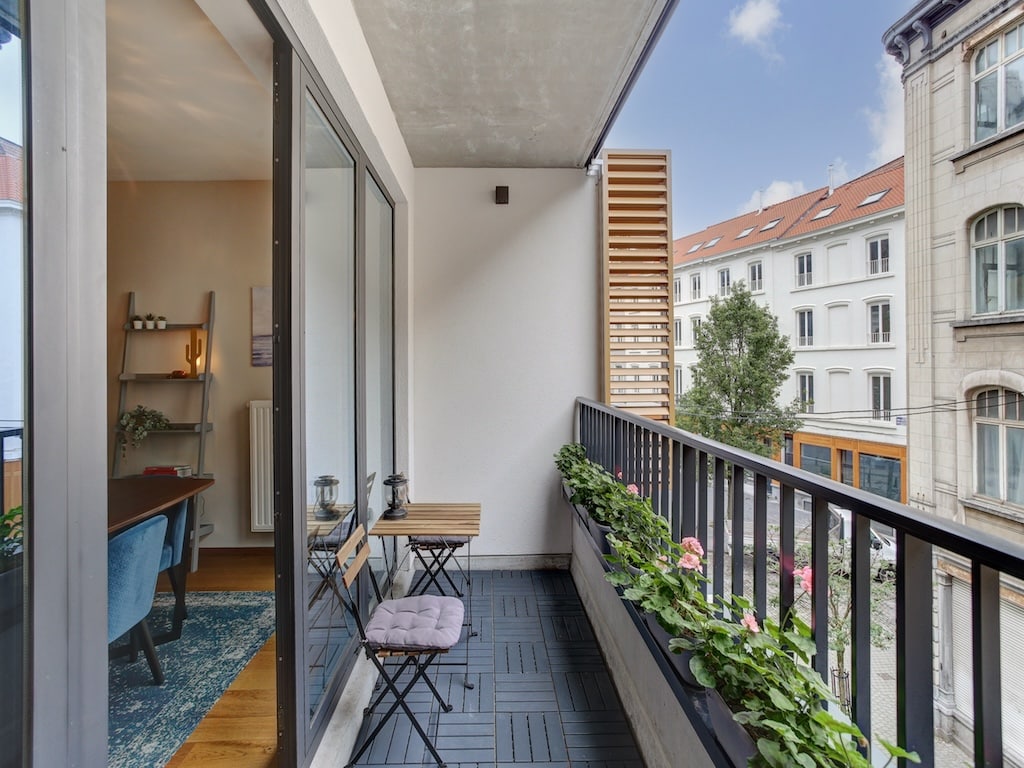 Balcon moderne avec plantes vertes, mobilier minimaliste et vue urbaine sur bâtiments anciens.