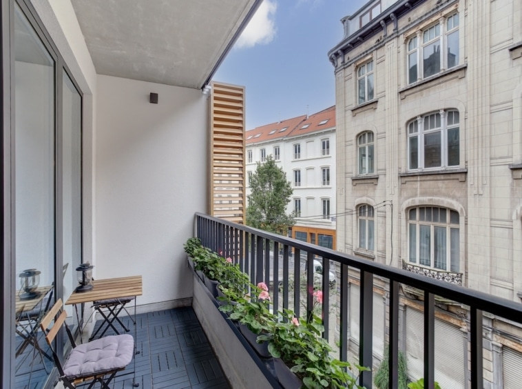 Balcon urbain moderne avec mobilier minimaliste, plantes colorées et vue sur la ville.