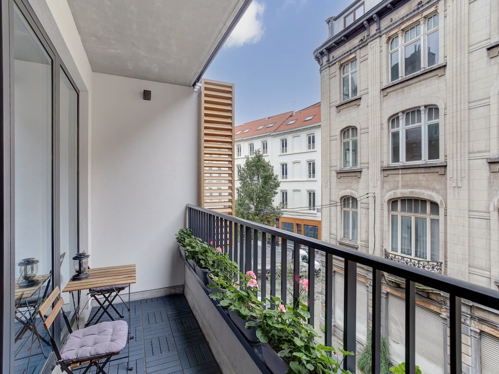 Balcon urbain moderne avec mobilier minimaliste, plantes colorées et vue sur la ville.