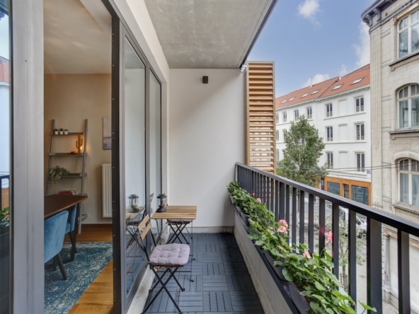 Balcon moderne avec plantes, fauteuil bleu, vue urbaine, lumière naturelle, ambiance zen et conviviale.