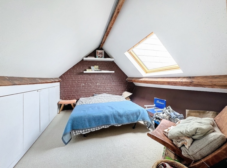 Chambre en attique cosy avec poutres, grande lucarne, lit bleu, ambiance rustique et chaleureuse.